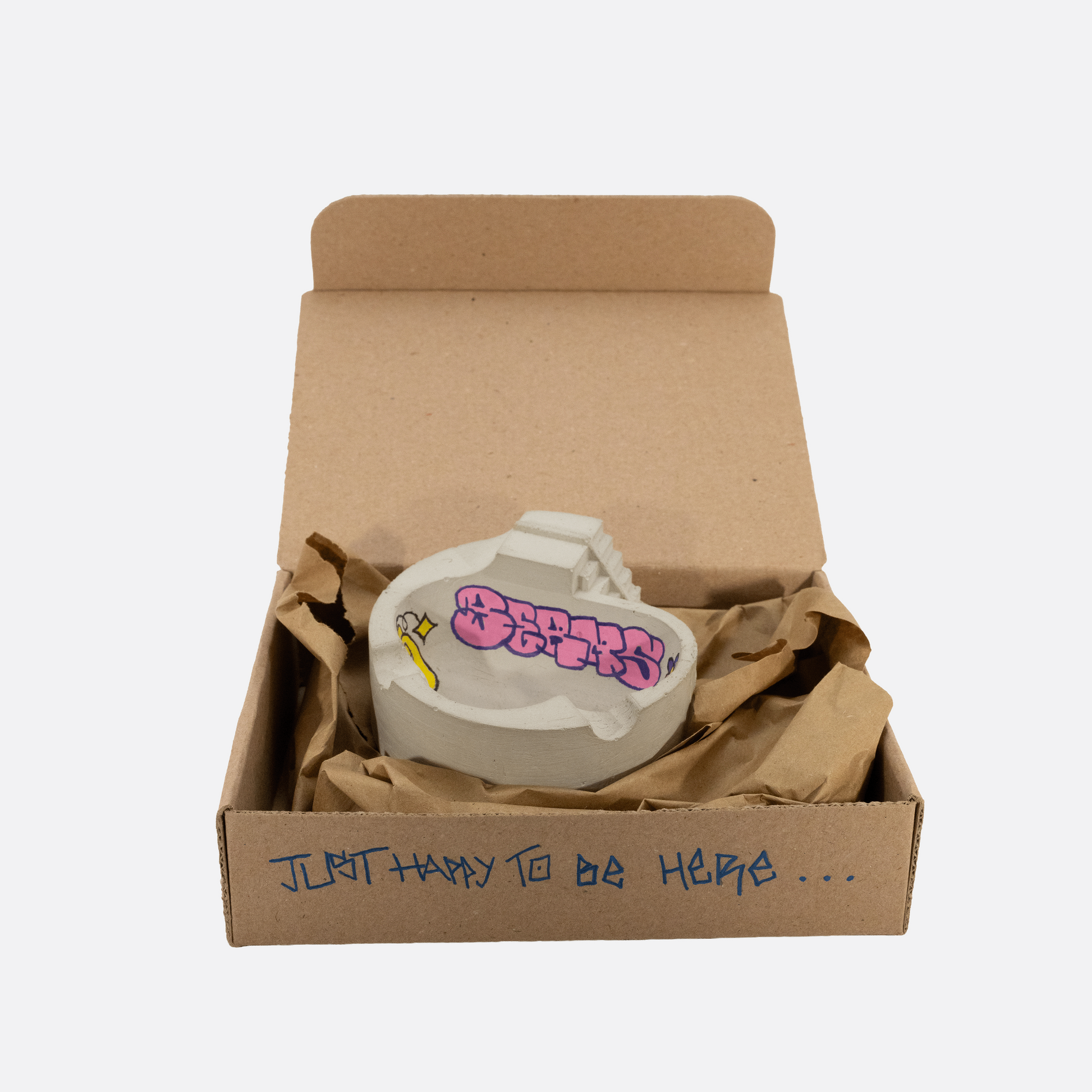 Small white container with pink text and yellow design inside an open cardboard box on a white background