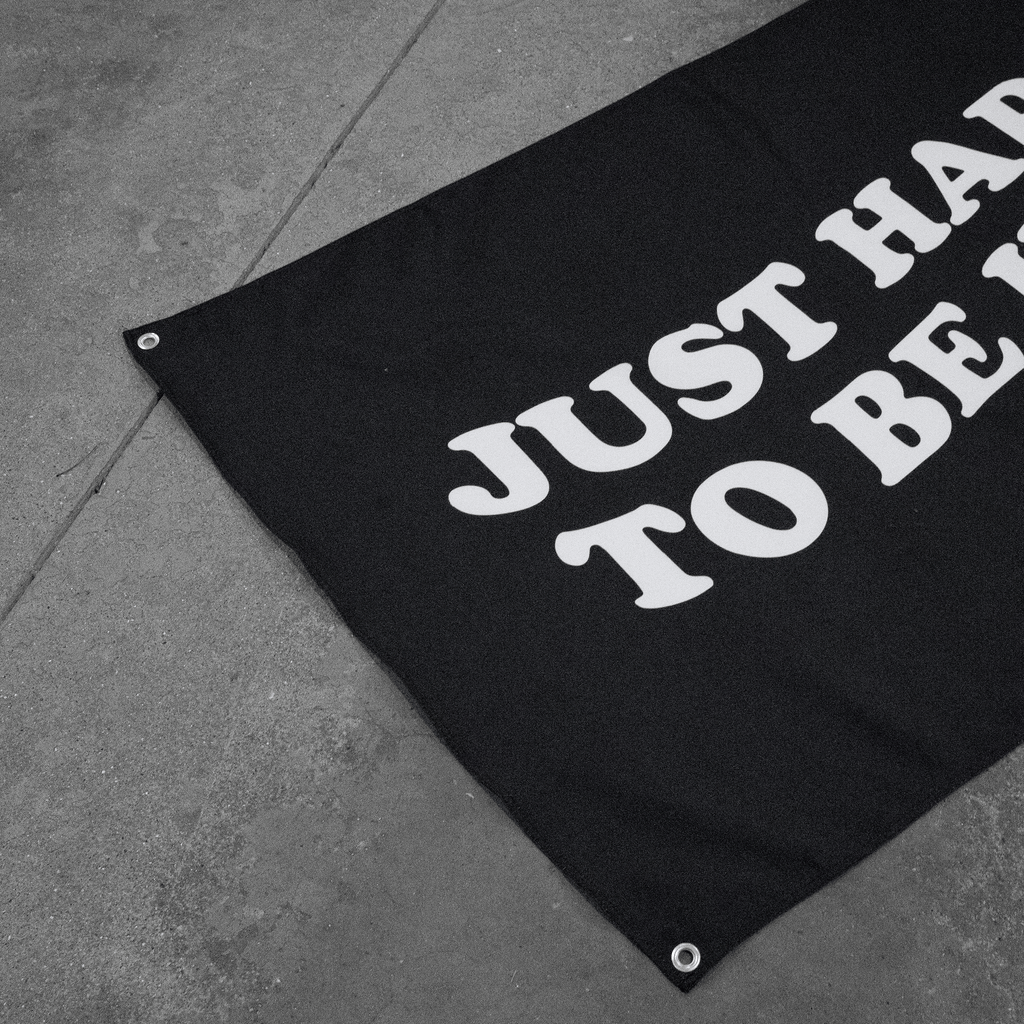 Black banner with 'JUST HAPPY TO BE HERE' text on a gray concrete floor.